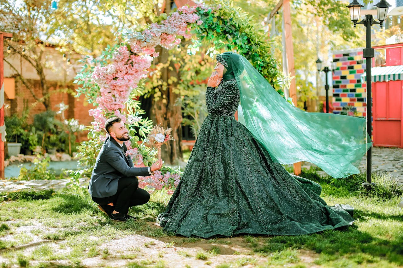 A man proposing to a woman in a green wedding dress with floral arch.